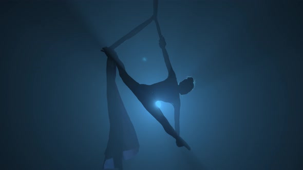 Silhouette of Graceful Aerial Gymnast Performing Acrobatic Stunts and Stretching on Aerial Silk