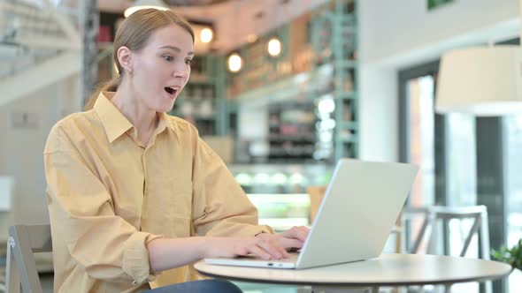 Young Woman Celebrating Success on Laptop in Cafe 