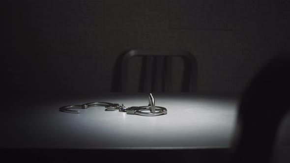 Medium tracking shot of a pair of handcuffs on a table in an interrogation room.