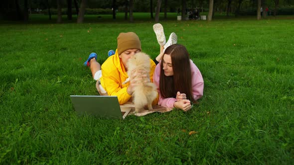 Young Guy and Girl Play with a Little Cute Dog Lying on the Grass in the Park