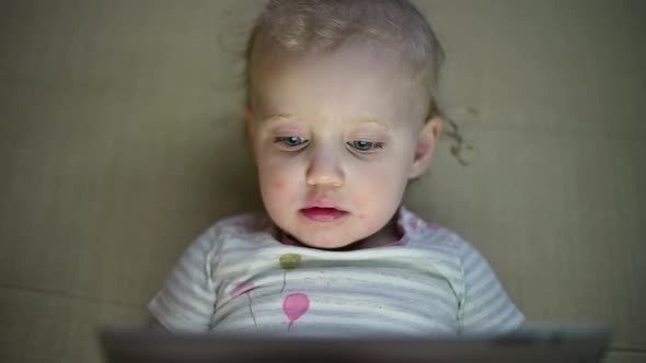 The little girl is fascinated by the screen of the tablet.