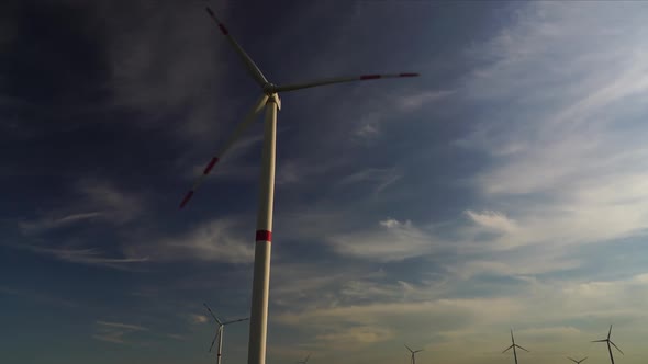 Blades of a Large Wind Turbine in a Field Against a Background of Cloudy Blue Sky on the Horizon