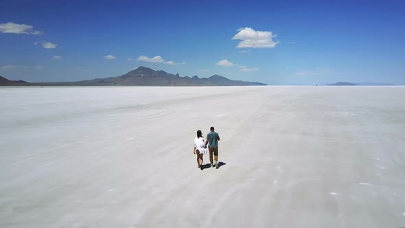 Drone Follows Romantic Couple Holding Hands, Walking Towards Epic White Flat Land in the Middle of