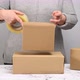 woman in a gray sweater holds a roll of duct tape and packs brown cardboard boxes  - VideoHive Item for Sale