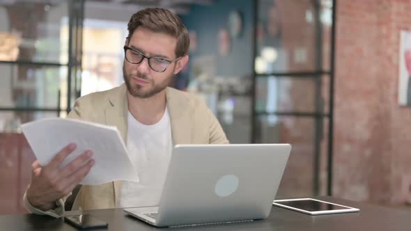 Man with Laptop Reading Documents