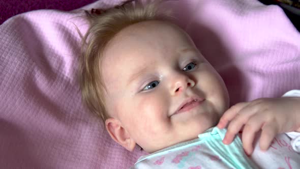 The Baby Is Lying on the Bed and Smiling. Face Close Up.