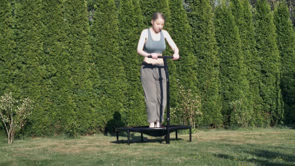 girl does Jumping fitness on trampoline in outdoor on green grass and trees on background