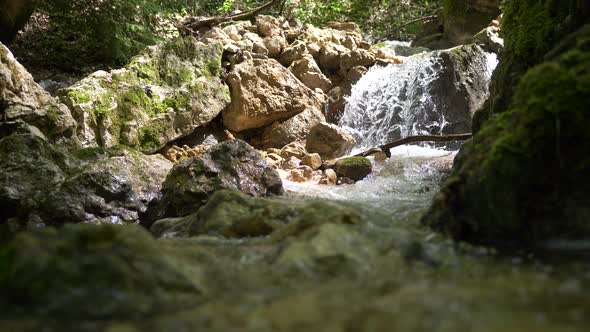 Low angle shot of small waterfall flowing between rocks in alp mountains during sunlight