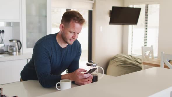 Caucasian man standing in kitchen and using smartphone