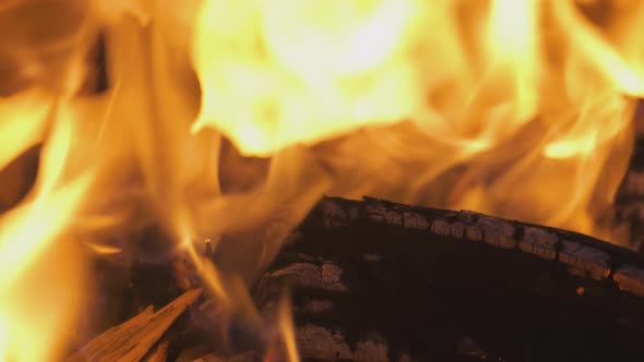 Close up of brightly burning wooden logs with yellow hot flames of fire at night.