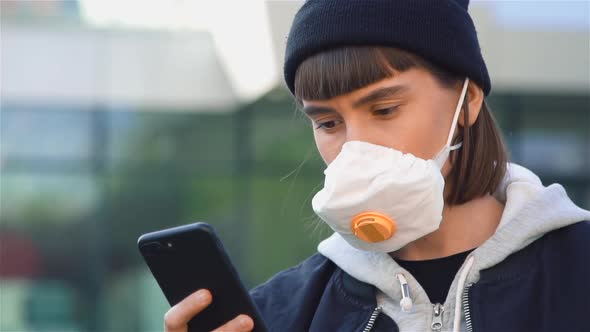 Close-up of Millenial Young Woman in Respiratory Mask Reading News in Phone