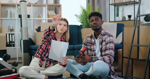 Young Multiracial Couple Sitting on the Floor in Own House and Discussing their Ideas