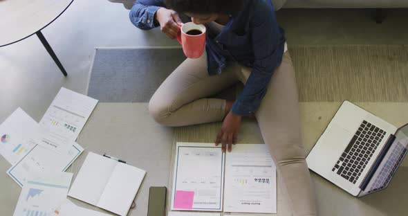 Happy african american woman sitting on floor, using laptop and working