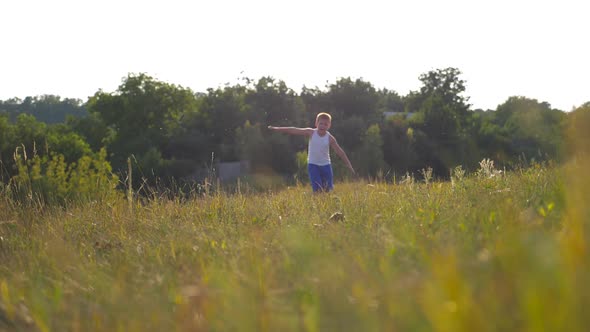 Young Boy with Raised Hands Running on Green Grass at the Field on Sunny Day