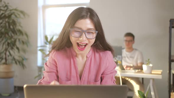 Beautiful Asian Businesswoman in Glasses Sitting at Her Office Desk in Front of Laptop Raising Arms