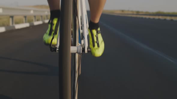 Closeup of the Legs of a Road Cyclist Riding on a Black Highway with a New Road. Cyclist's Feet in