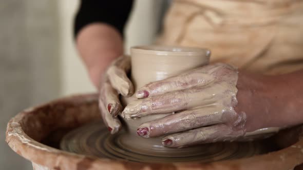 Closeup of Potter's Dirty Hands Working with Wet Clay on a Pottery Wheel Making a Vase in a Workshop