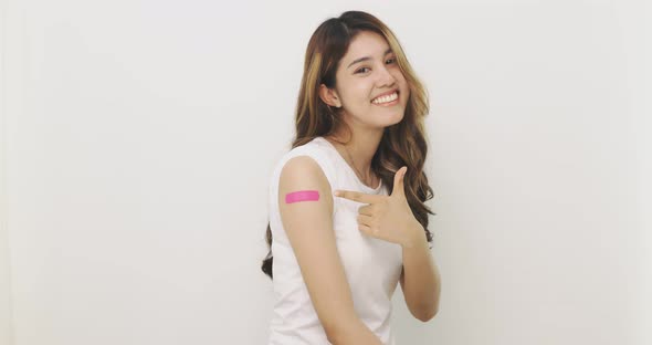 Asian Woman Points To Bandage On Arm. Happy Asian Woman Feels Good After Received Vaccine.