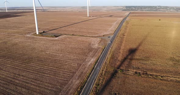 Car Traveling On Country Road Passing By Wind Turbines On Sunset. Aerial Drone
