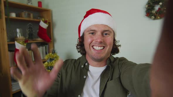 Happy caucasian man in santa hat on christmas video call waving and talking