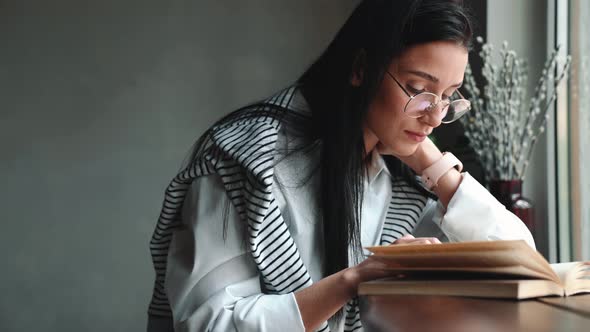 Handsome young brunette woman in eyeglasses reading book