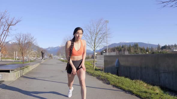 Latina Runner Stops to Catch Breath with Hands on Knees in Orange Sports Bra