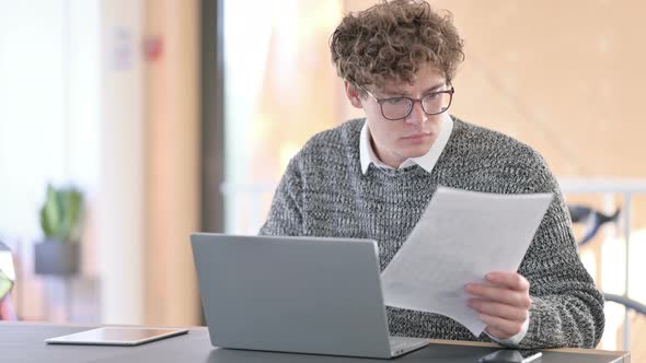 Young Man with Documents Working on Laptop