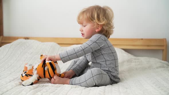 little boy of two years old plays with toy tiger on the bed