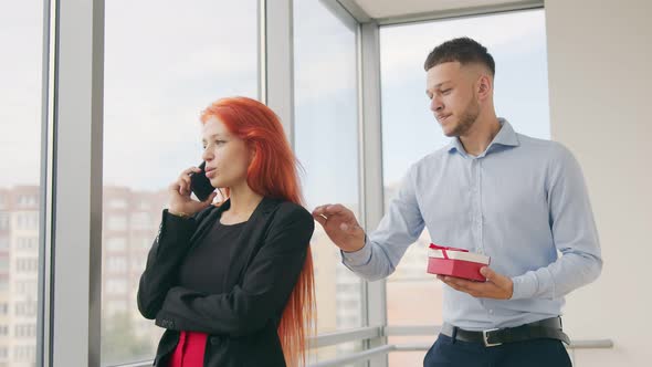 A Man Gives a Gift To a Woman with Red Hair. A Woman Who Speaks on the Phone Receives a Gift From