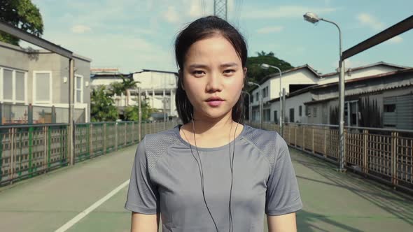 Attractive young Asian woman looking at camera wearing earphones listening to music.