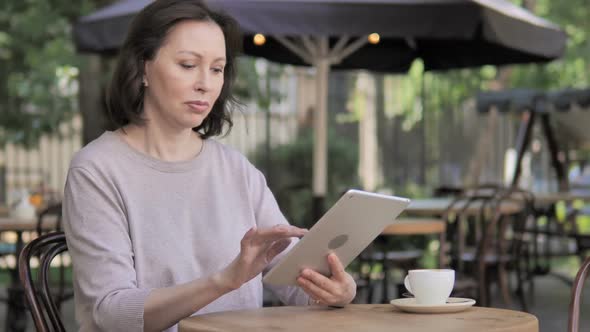 Old Woman Using Tablet Sitting in Outdoor Cafe