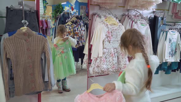 Baby Holds Rack with Dresses in Emporium