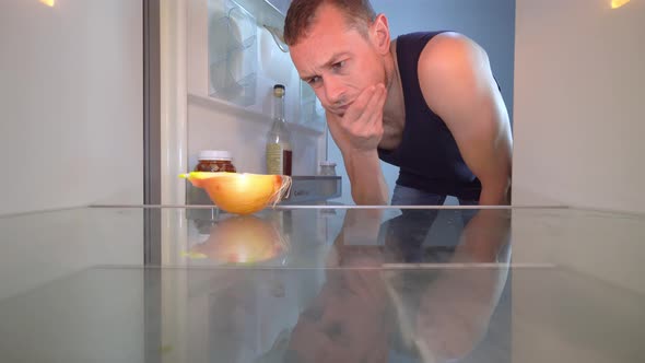 man looks into refrigerator, looks at onion and takes a bottle of alcohol.