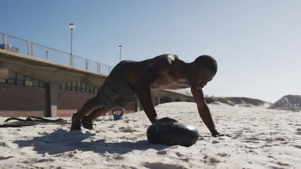 Focused african american man doing press ups on ball, exercising outdoors on beach