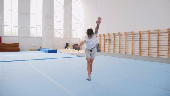 A Teenager Boy is Doing a Cartwheel and a Triple Back Flip in Gym Steadicam