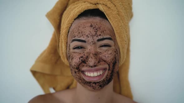 Young smiling woman applying coffee scrub mask with brush on face