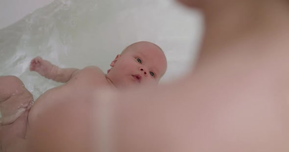 The Cute Newborn Tries to Swim on Back in the Bath with Mother Help