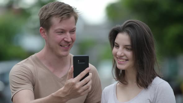 Young Happy Couple Using Phone Together in the Streets Outdoors