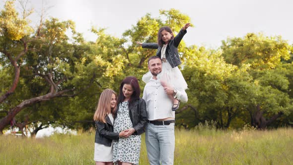 Pretty Woman in Expectation Standing with Her Lovely Husband and Two Daughters