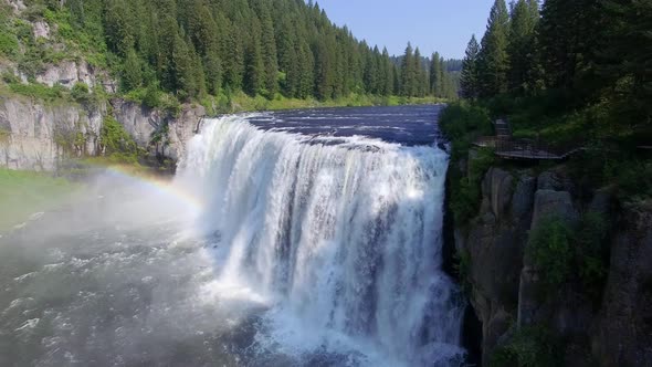 Water cascades down a water fall as the camera glides forwards and a rainbow in the mist