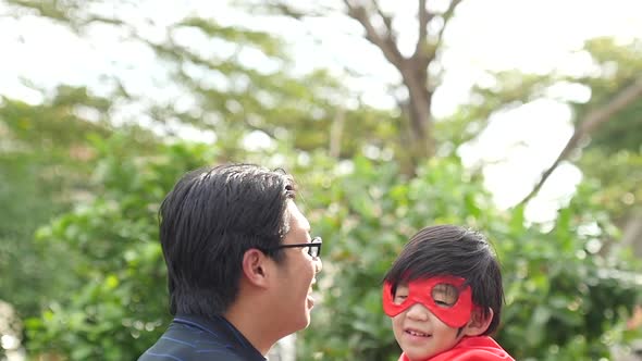 Asian Father And His Son Playing Superhero Together In The Park