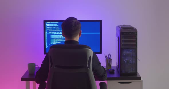 Rear View of Man Programmer Coding Network Security Software Indoors in Neon Lights at Night