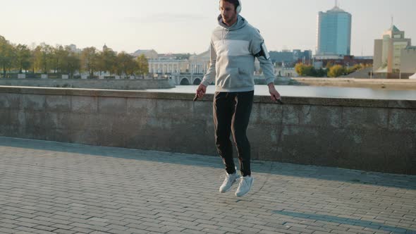 Slow Motion of Young Sportsman Wearing Headphones Jumping with Skipping Rope Exercising Alone