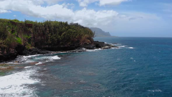 Aerial footage of ocean and coastal cliff with trees. Mountains on the horizon (Kauai, Hawaii, USA)