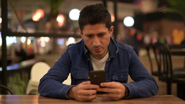 Hispanic Man Thinking While Using Phone at the Restaurant