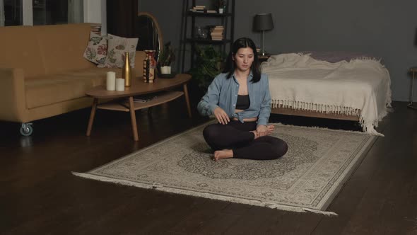 Relaxed young Asian woman in sportswear is meditating in lotus position sitting on floor with closed