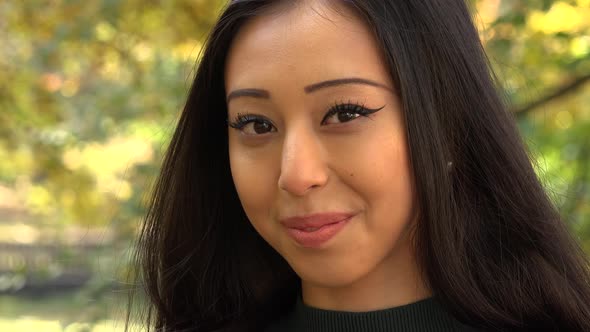 A Young Asian Woman Smiles at The Camera in A Park