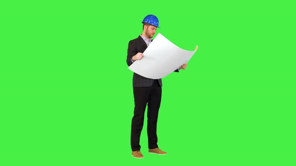 Male Builder Engineer Architect in Hard Hat Reading Blueprint Focused Work on Building Plan Draft on