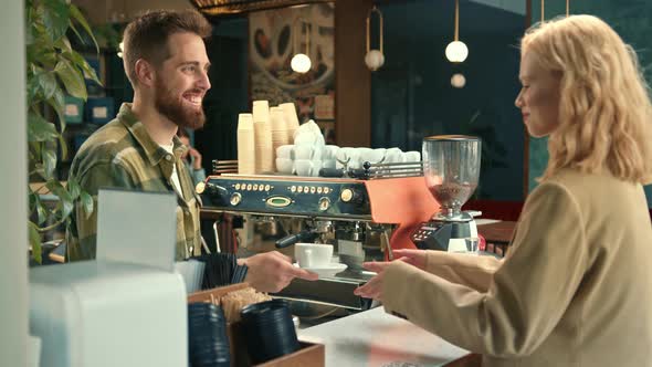 Handsome male barista gives coffee to a girl. Girl buys coffee in a coffee shop.