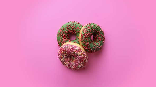 Composition of Three Rotating Sweet Donuts with Multicolored Sprinkle Glazed Isolated on Pink